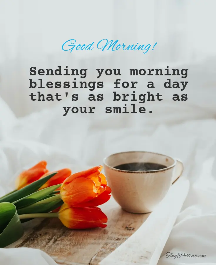 A 'Good Morning' blessing text displayed over a photo of a wooden tray with orange tulips and a steaming cup of coffee on a bed.